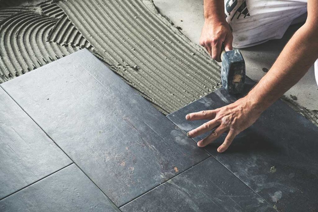 Person dust-mopping a sunny hardwood floor in a lived-in home with visible entryway mats and rugs