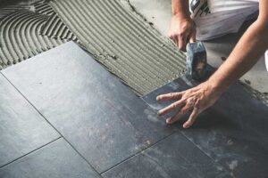 Person dust-mopping a sunny hardwood floor in a lived-in home with visible entryway mats and rugs