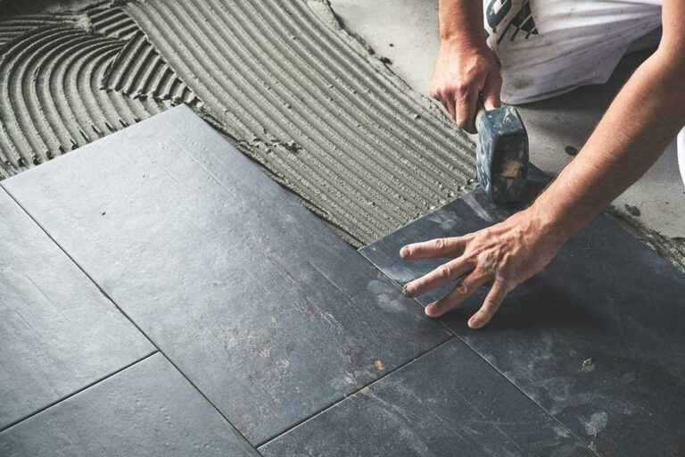 Person dust-mopping a sunny hardwood floor in a lived-in home with visible entryway mats and rugs